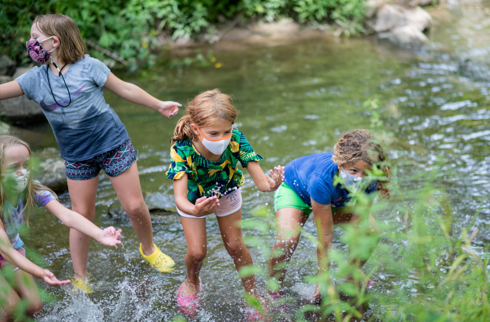 Kids at summer camp with masks splashing in the creek