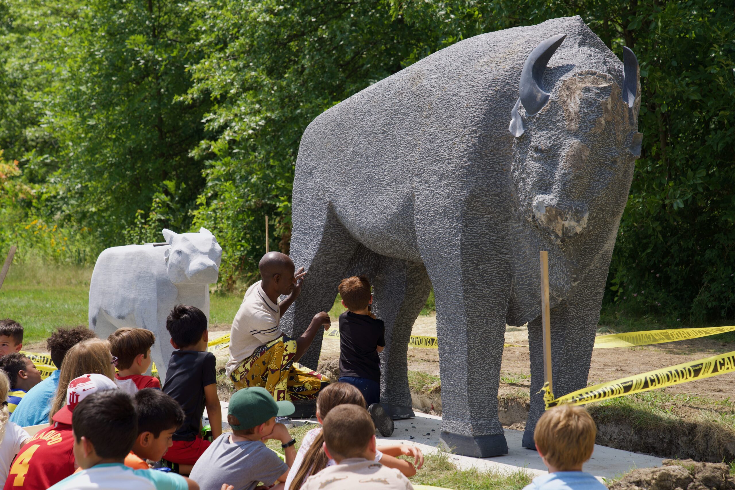 Artist, Dominic Benhura, working on his sculpture alongside kids from summer camp.