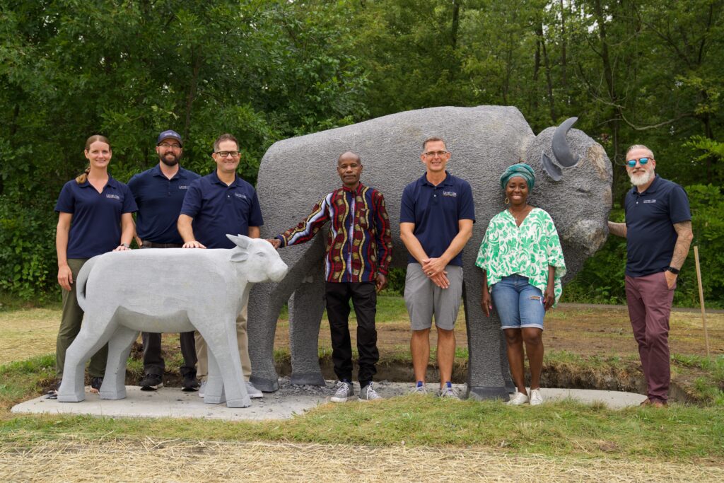 Group photo in front of the Bison & Calf sculpture featuring artist Dominic Benhura, the sculpture's sourcer, and CCPR employees.